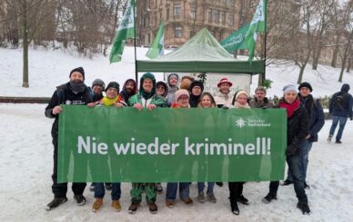 Bild zeigt Aktivisten mit Banner "Nie wieder Kriminell" vor Gerichtsgebäude im Winter.